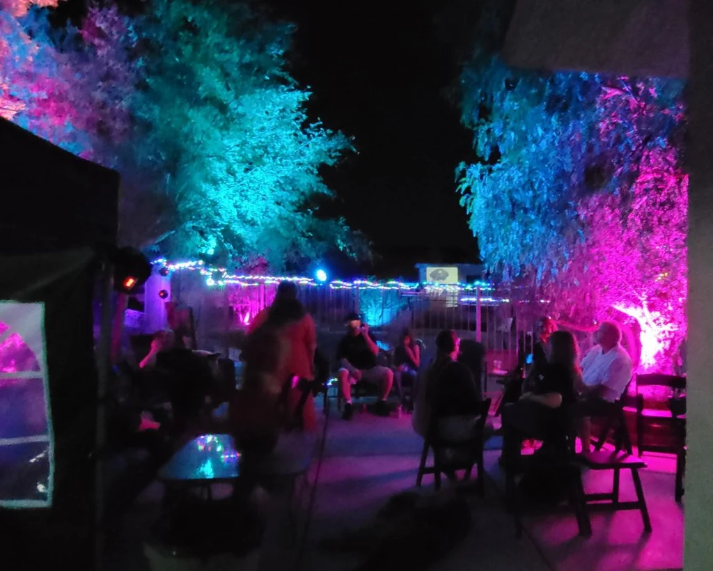 Guests gathered beside an event tent under cyan and magenta tree lighting.