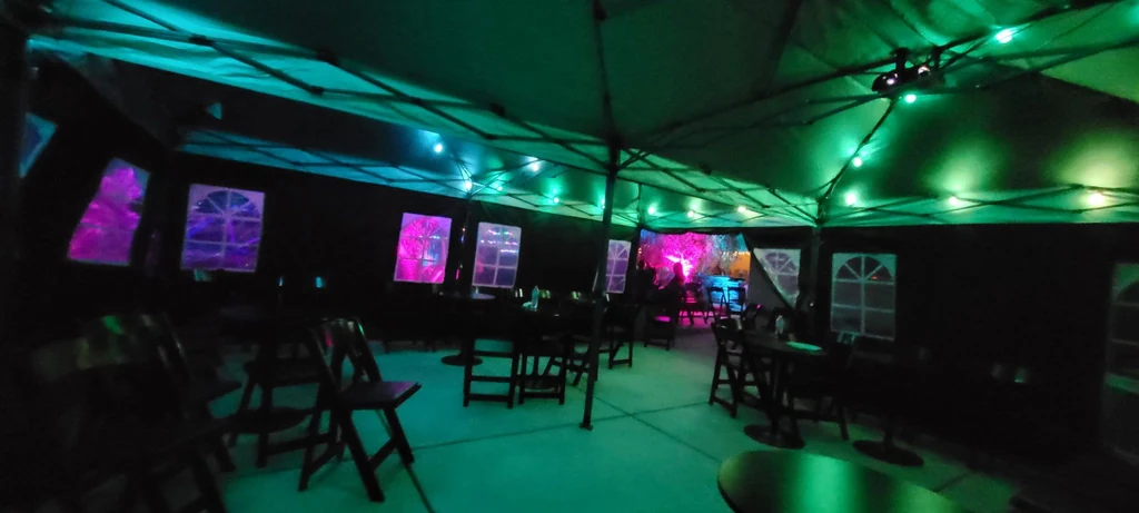 Tented event space with tables, chairs, string lights and green and cyan lighting.