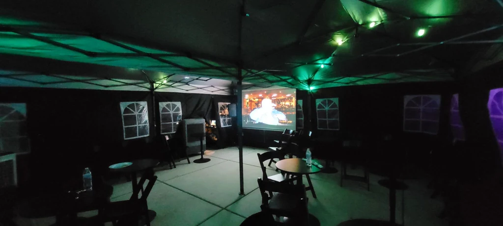Event tent with cocktail tables, seating, colored lighting, a cooling unit and video projection.
